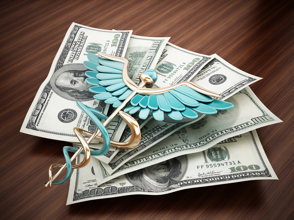 Stack of hundred-dollar bills with a metallic caduceus symbol on top representing healthcare finances and savings