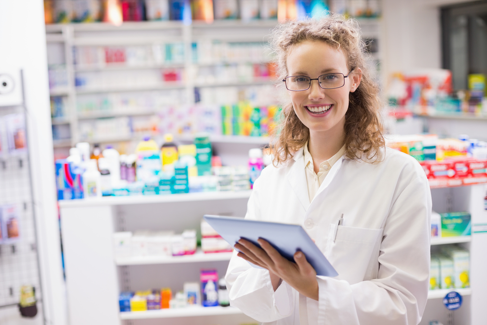Pharmacist using a tablet in a well-stocked pharmacy, illustrating modern pharmaceutical service and care
