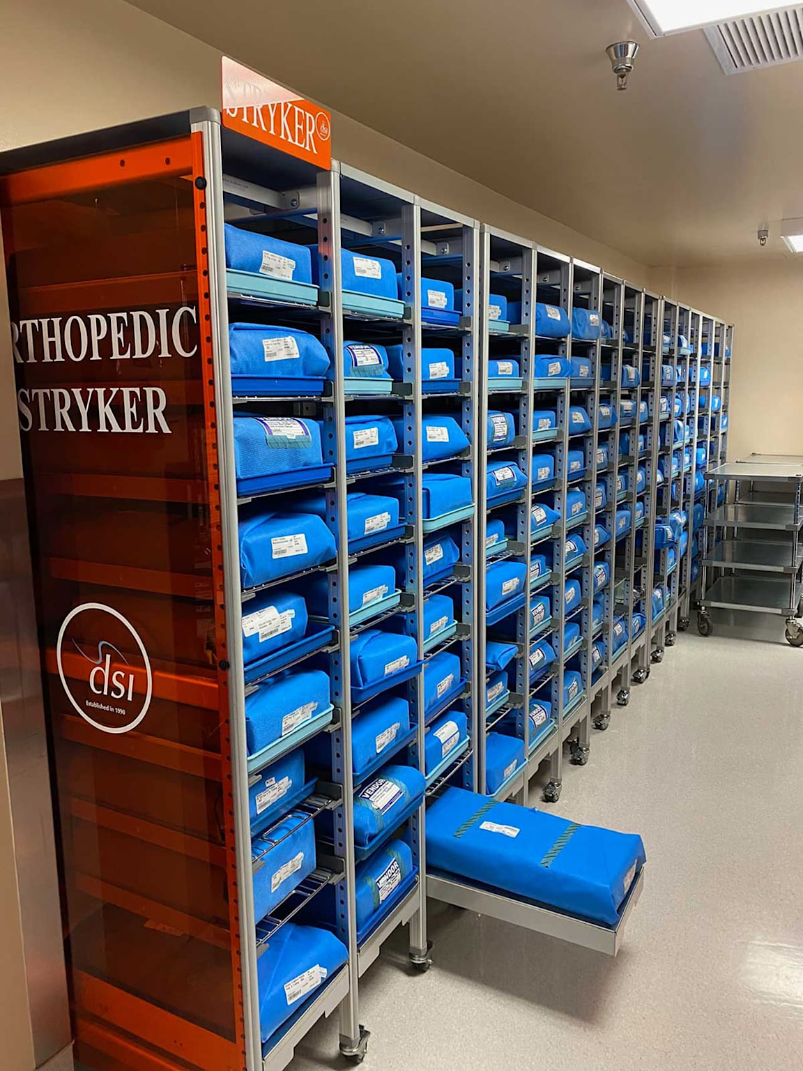 Shelving units with labeled blue surgical supply packs neatly organized in a medical storage room