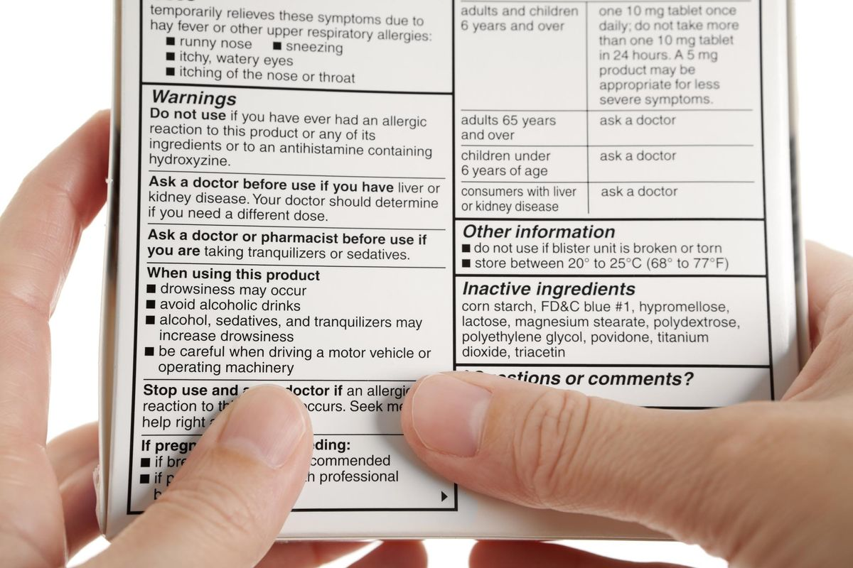 Close-up of a person reading medication warning labels and dosage instructions on an OTC drug box