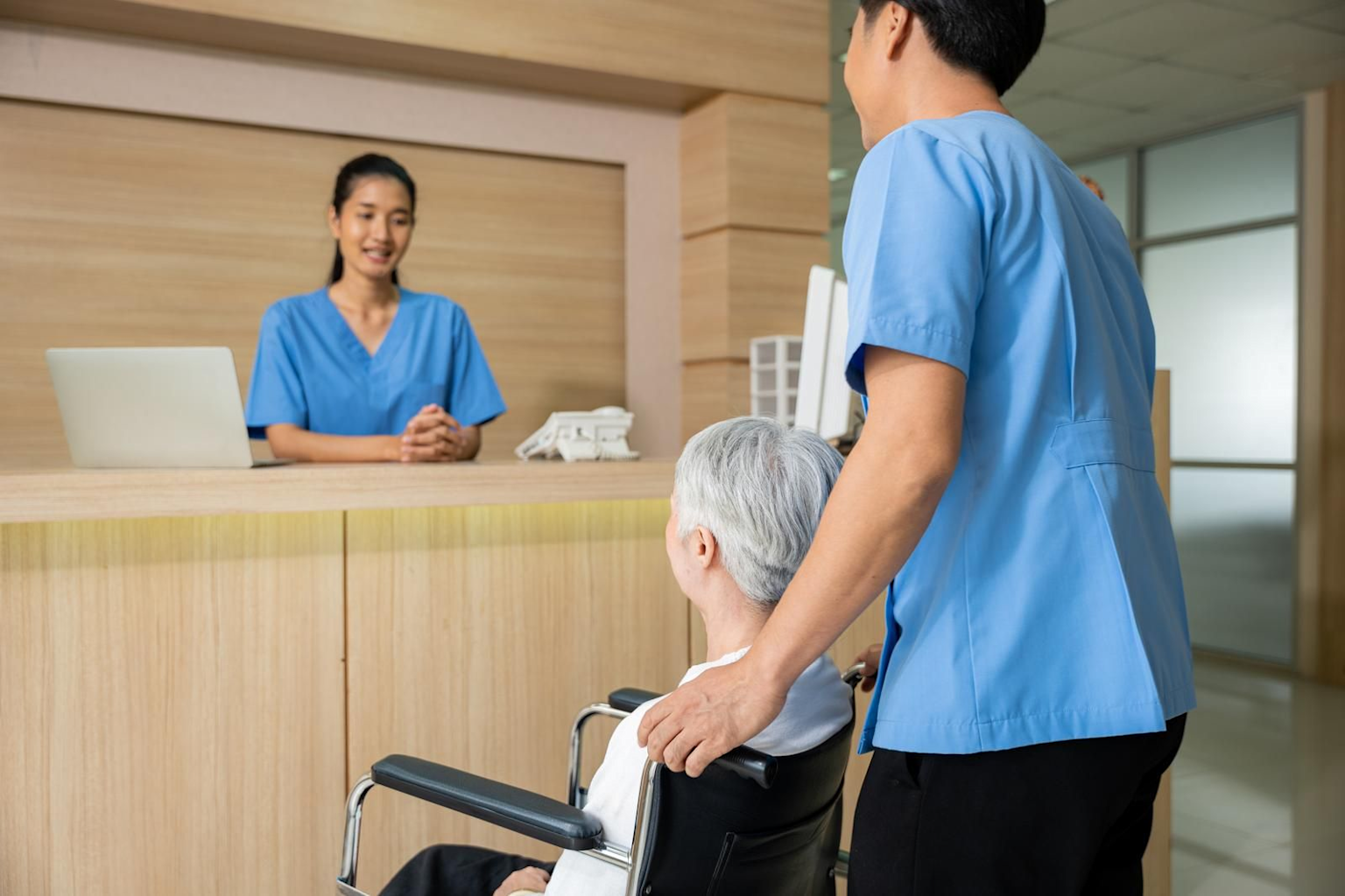 Medical staff assisting an elderly customer in a wheelchair at a healthcare reception desk