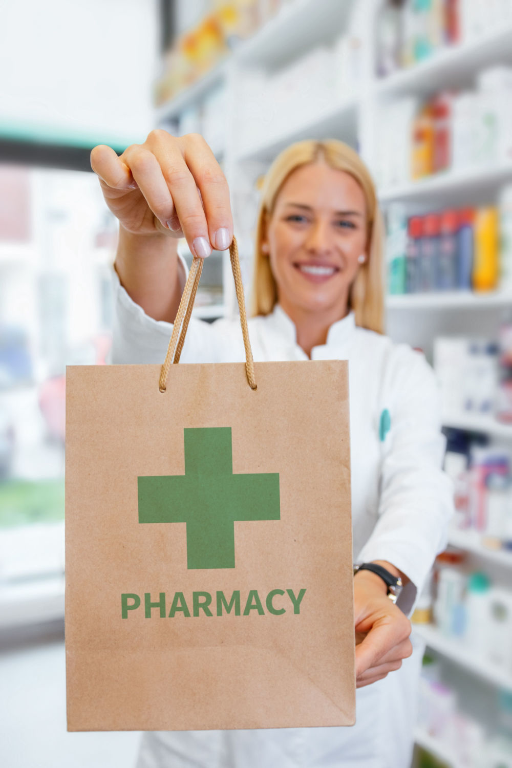 Pharmacy staff holding brown paper bag with green pharmacy cross symbol